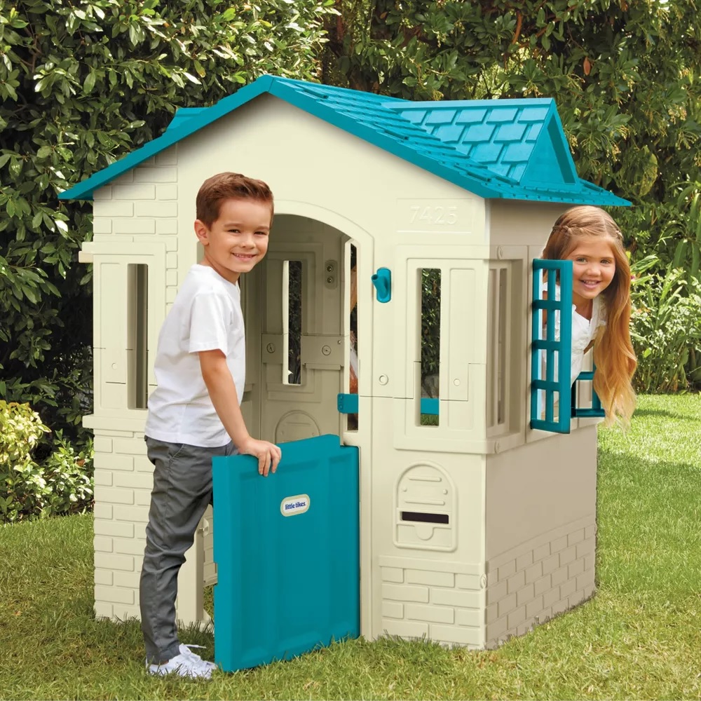 A playhouse with a blue roof and a boy and girl peeking out from it.