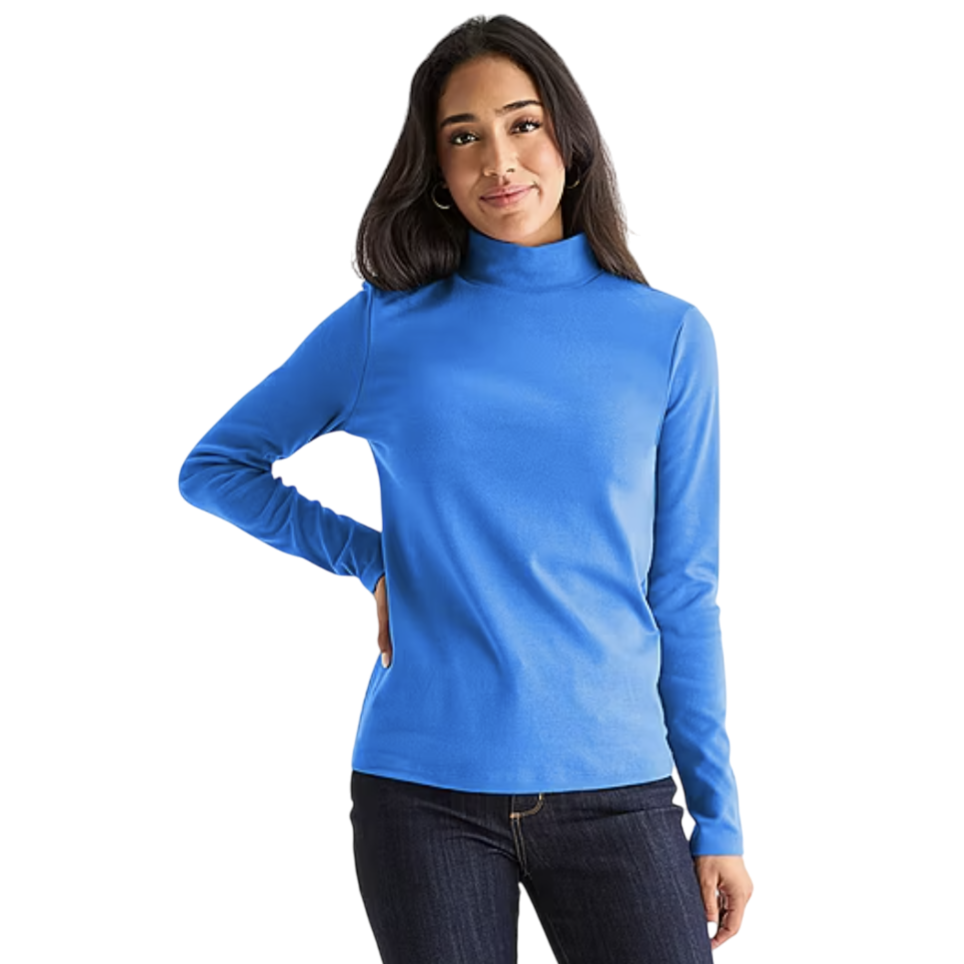 A woman is wearing a bright blue turtleneck and dark blue jeans, posing with one hand on her hip.