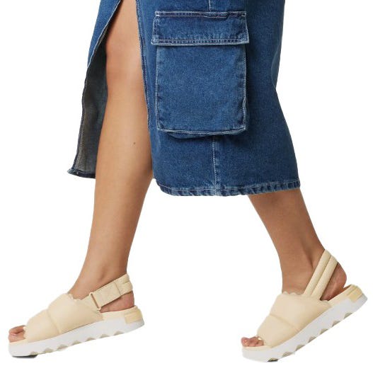 A person is wearing beige platform sandals with a chunky sole and a denim skirt that features a large side cargo pocket and a front slit.