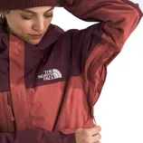 A person wearing a The North Face jacket in shades of maroon and pink, adjusting the hood with a beanie.