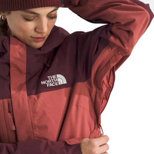 A person wearing a The North Face jacket in shades of maroon and pink, adjusting the hood with a beanie.