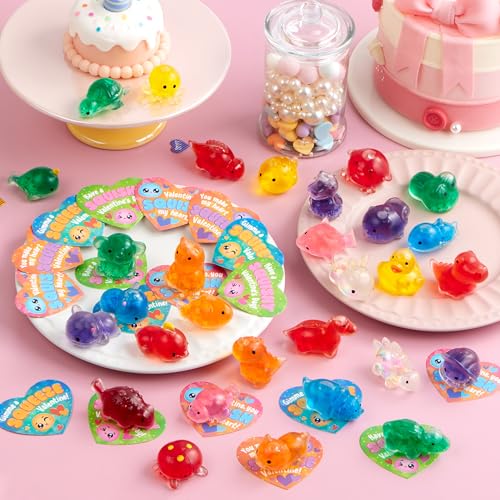 A collection of colorful, translucent animal figurines displayed on a pink background with heart-shaped cards, accompanied by decorative cake figures and a jar of pastel-colored candies.