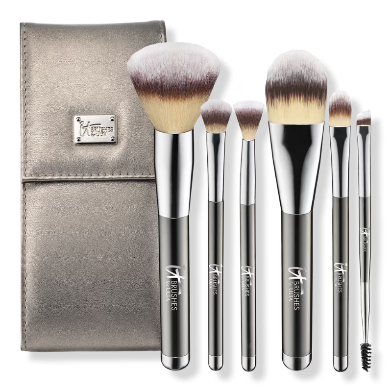 A set of six makeup brushes with metallic handles and a matching metallic case, featuring a variety of brush types including a large powder brush, foundation brush, and spoolie.