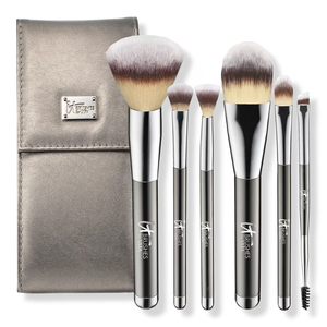A set of six makeup brushes with metallic handles and a matching metallic case, featuring a variety of brush types including a large powder brush, foundation brush, and spoolie.