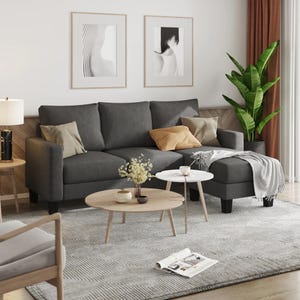 Gray sofa with matching ottoman, round wooden coffee table, side table with lamp, framed artwork, potted plant, and decorative items.