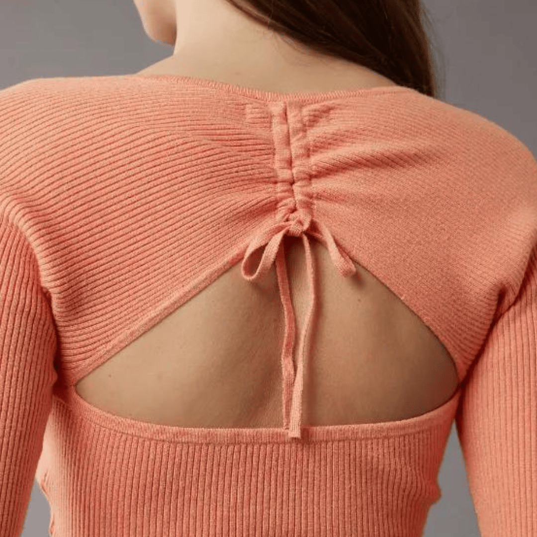 A coral pink knitted sweater with an open back tied at the neckline.