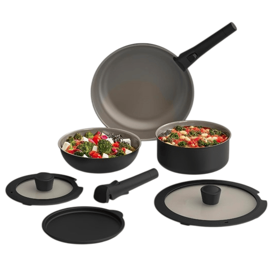 Cookware set with detachable handle, including a frying pan, two pots with glass lids, and a storage lid. Contains colorful vegetable dishes inside the pots.