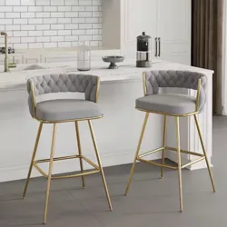 Two bar stools with gray cushioned seats and tufted backs, featuring gold metal frames, are positioned in a modern kitchen setting.