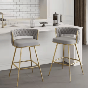 Two bar stools with gray cushioned seats and tufted backs, featuring gold metal frames, are positioned in a modern kitchen setting.