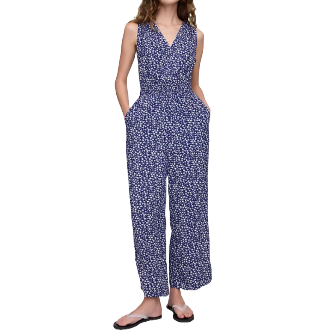 A sleeveless, V-neck jumpsuit with a smocked, elasticized waist and a wide-leg design, featuring a blue fabric with a white floral pattern.
