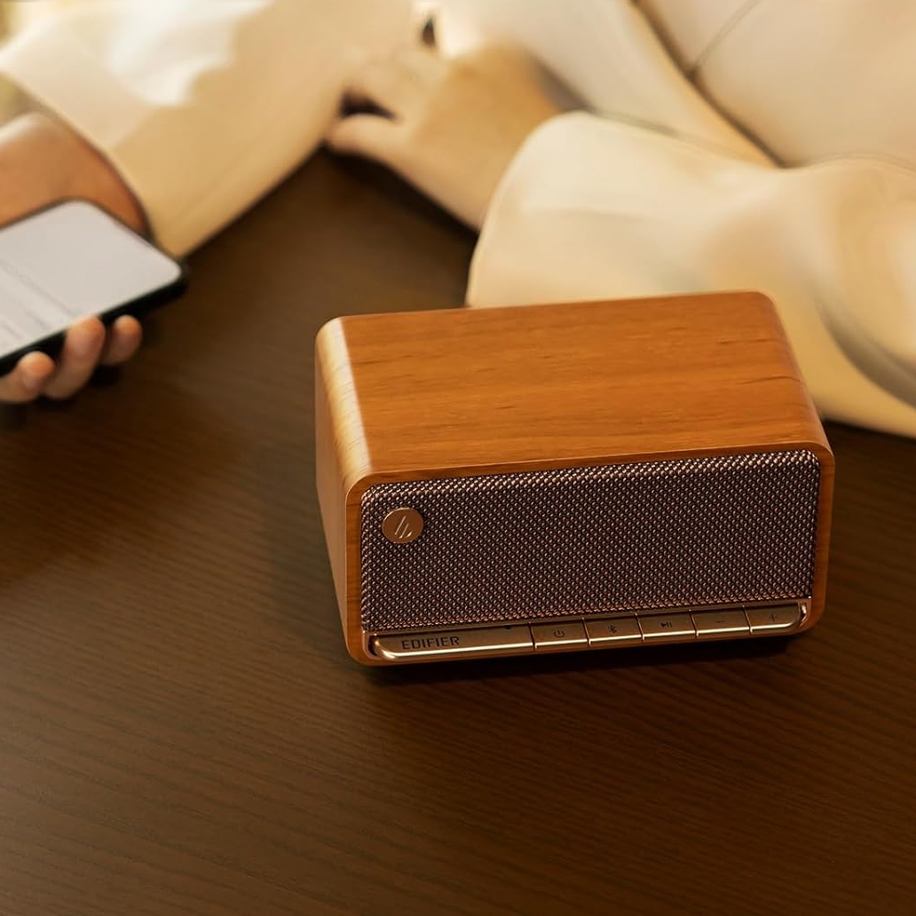 A wooden retro-style Bluetooth speaker on a table next to a person holding a smartphone.