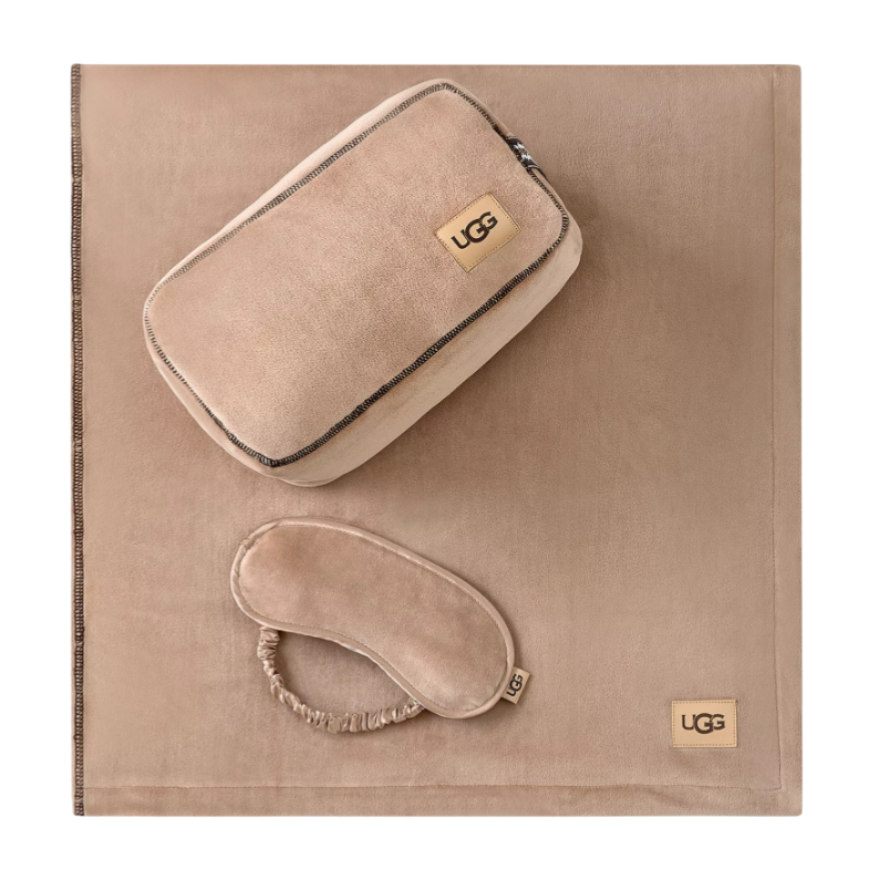 A tan travel set featuring a blanket, an eye mask, and a zippered pouch, each branded with the UGG logo.