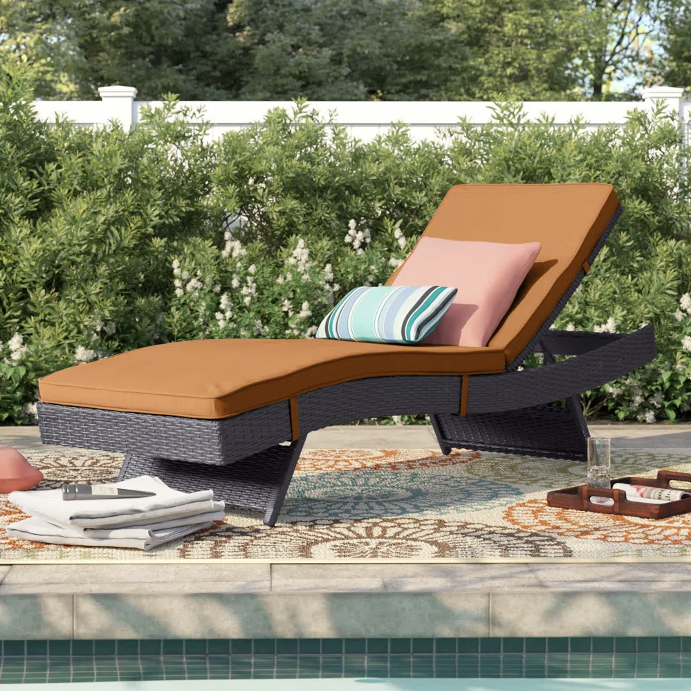 Poolside lounge chair with a brown cushion and two pillows, one striped and one solid. It sits on a patterned outdoor rug beside a pool, surrounded by greenery.