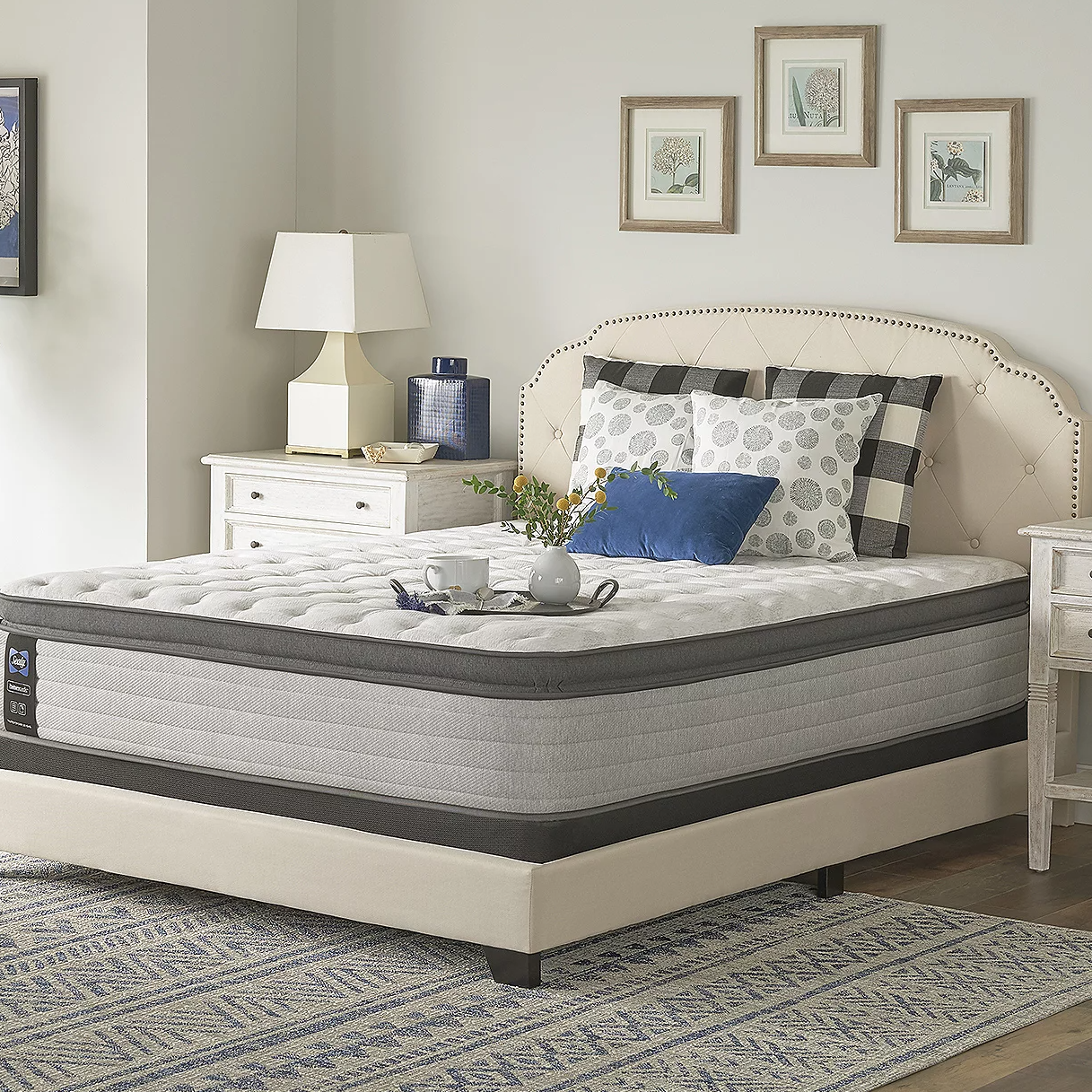 A bedroom setting with a bed featuring a plush mattress, upholstered headboard, and a nightstand with a lamp.