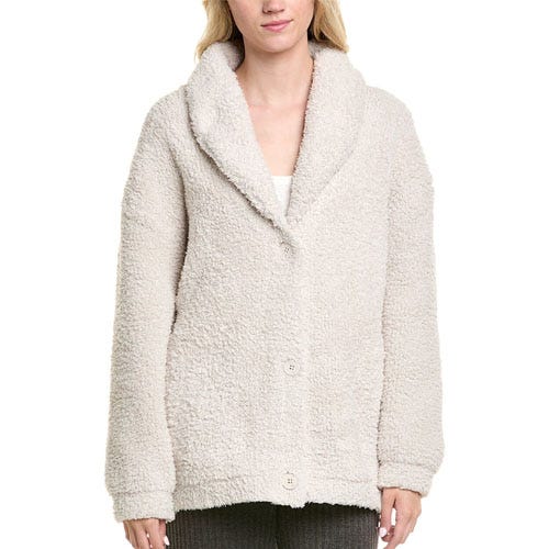 A woman is wearing a cream-colored, fuzzy, sherpa-style jacket with a shawl collar and button closure.
