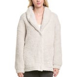 A woman is wearing a cream-colored, fuzzy, sherpa-style jacket with a shawl collar and button closure.