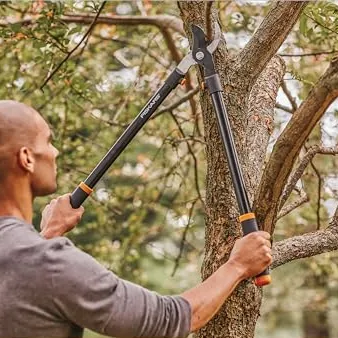 Man trimming a tree branch with Fiskars loppers featuring steel construction for durability.