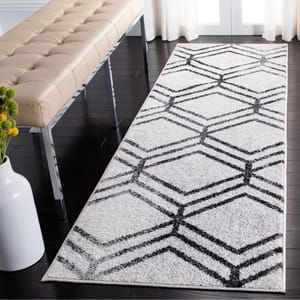 A white runner rug with a black geometric pattern is placed on a dark wooden floor, next to a beige tufted bench with chrome legs. A white vase with yellow flowers is visible in the foreground.