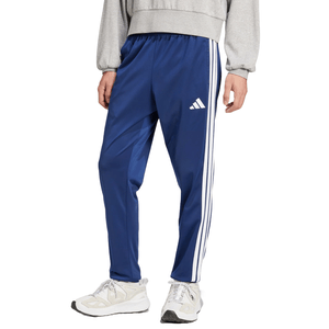 Blue Adidas Tricot Track Pants featuring white stripes down the sides and the Adidas logo on the left. They have an elastic waistband and are paired with white sneakers.