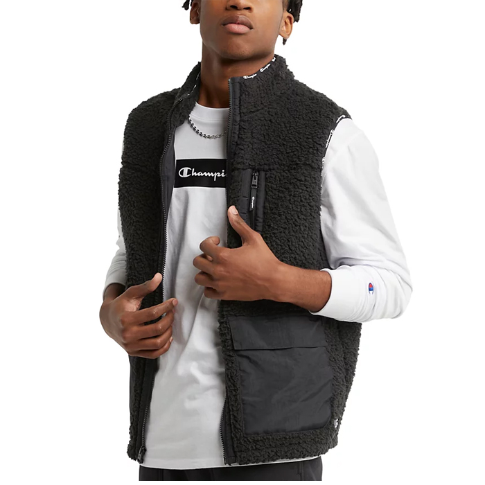 A man wearing a black fleece vest over a white long-sleeve shirt with the Champion logo.