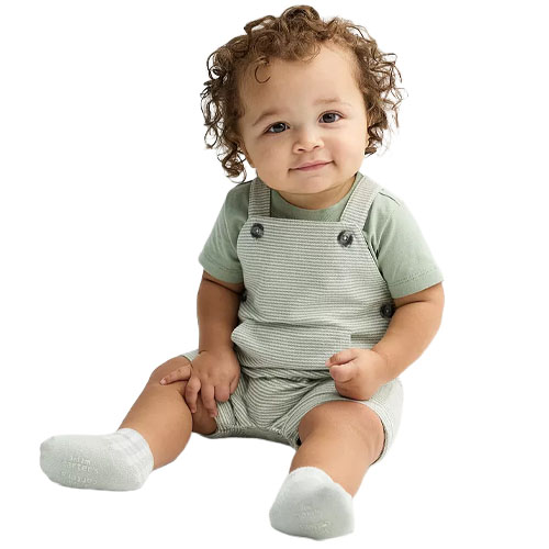 A baby wearing a light green short-sleeve shirt and striped overalls, with white socks, is sitting on a white background.