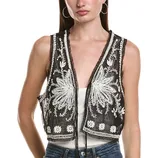 A woman is wearing a sleeveless, black mesh vest with intricate white embroidery over a white top and jeans.