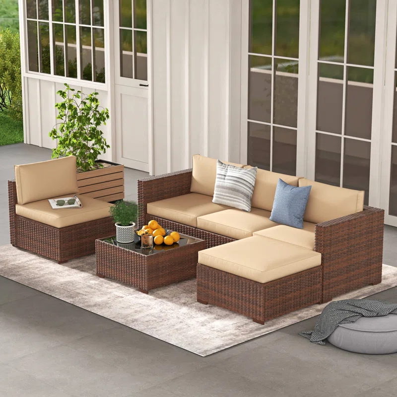 An outdoor furniture set with a brown rattan finish, beige cushions, and accent pillows placed on a gray area rug.