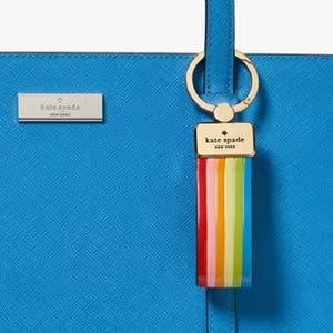 A blue Kate Spade New York bag features a colorful rainbow-striped keychain and a metal logo plaque.