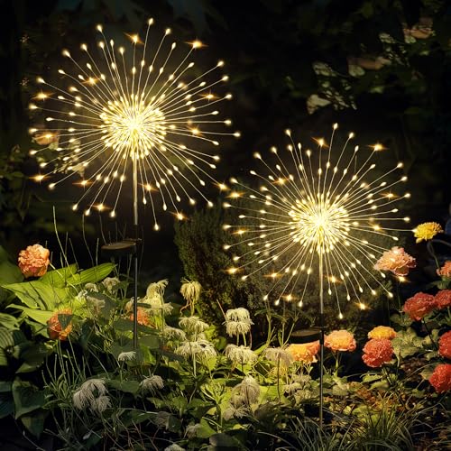 LED garden lights shaped like firework bursts illuminate a garden at night, surrounded by various flowers and plants.