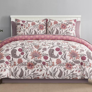 A bedding set featuring a floral pattern in pinks and purples, including a comforter and two matching pillow shams. The comforter is reversible, showing a different design on the inner side in similar color tones.