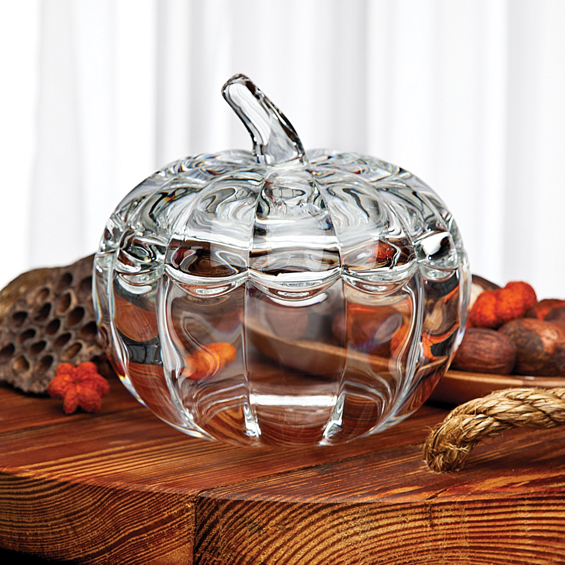 A clear glass pumpkin-shaped container with a removable lid on a wooden surface.