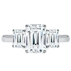 Three-stone ring with an emerald-cut center diamond flanked by two smaller emerald-cut diamonds, all set in a sleek metal band.