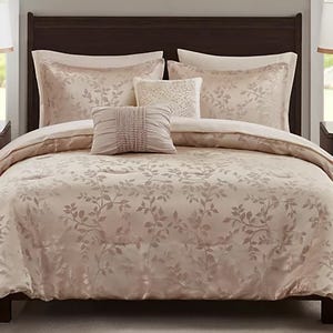 A floral-patterned bedding set featuring a comforter, two large pillows, and two decorative throw pillows, all in a soft beige tone.