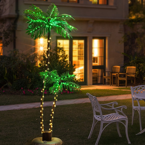 6' LED Artificial Palm Tree Set features illuminated palm trees with green and warm white lights, suitable for outdoor decoration. The trees are positioned on a lawn with chairs and a building in the background.