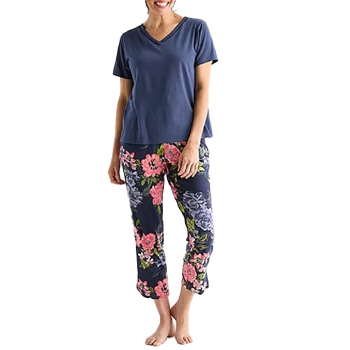 A person wearing a blue V-neck T-shirt paired with floral-patterned capri pants standing barefoot.