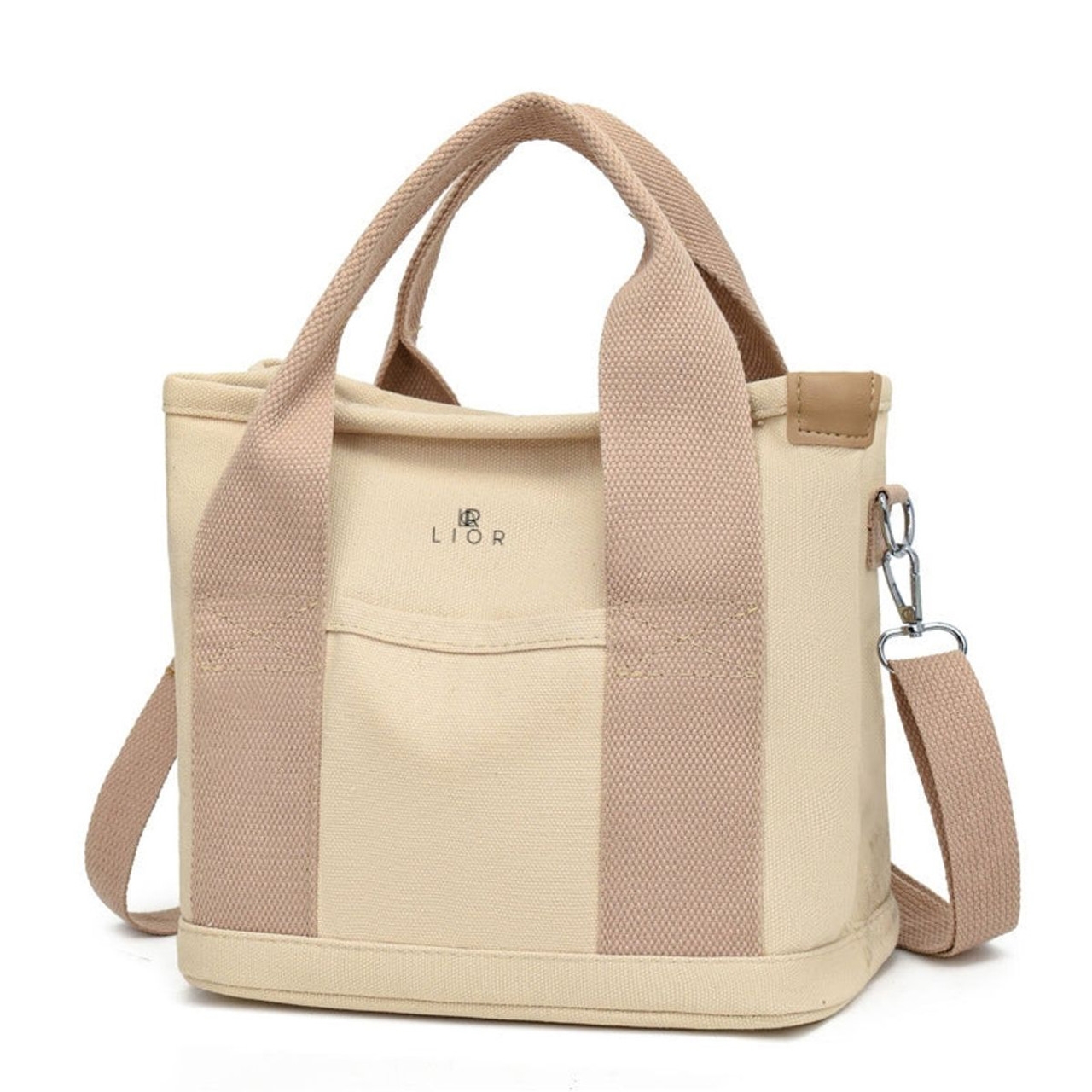 Beige canvas tote with tan handles and an adjustable strap, featuring a front pocket and metal hardware. The brand name \“LIOR\“ is printed on the front.