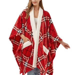 A woman is wearing a red plaid poncho with white sherpa lining and pockets.
