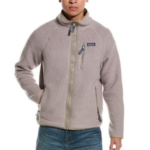 A person is wearing a beige fleece jacket with a chest zipper pocket and two side zipper pockets, paired with jeans.
