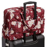 A maroon quilted floral-patterned bag with a handle is attached to the extended handle of a black suitcase. The bag features two carry handles and a zip closure.