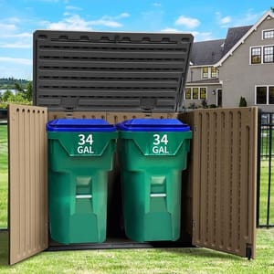A double-door outdoor storage shed houses two green 34-gallon trash bins with blue lids, set in a backyard with a house and yard in the background.