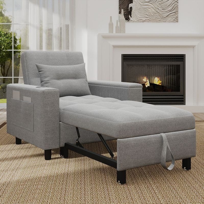 Grey convertible recliner chair with a pull-out footrest, pillow, side pocket, and black metal support, placed on a woven rug in front of a fireplace and a window with sheer curtains.