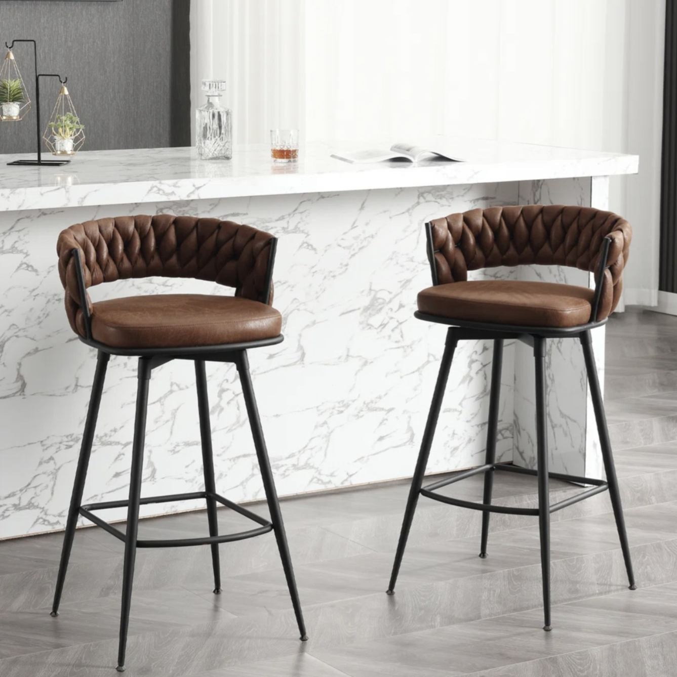 Two brown leather barstools with quilted backs and black metal legs are placed in front of a countertop with a white marble finish.