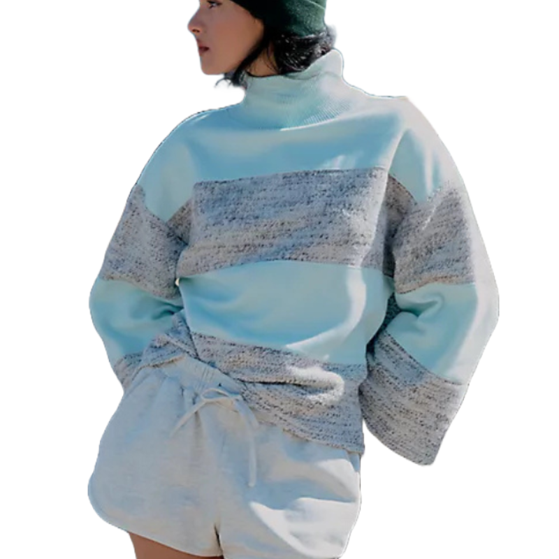 A woman is wearing a light blue and gray color-block long-sleeve poncho with a turtleneck and loose fit, paired with drawstring shorts and a green beanie.