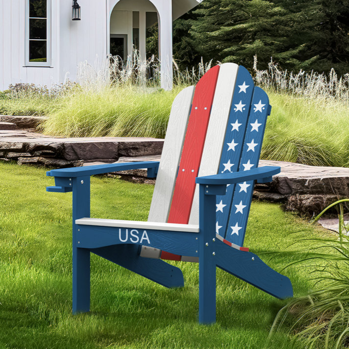 Adirondack chair with a patriotic USA design sits on a lawn in front of a white house surrounded by greenery.