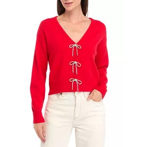 A red V-neck cardigan with three bow ties down the front and long sleeves, paired with cream-colored pants.