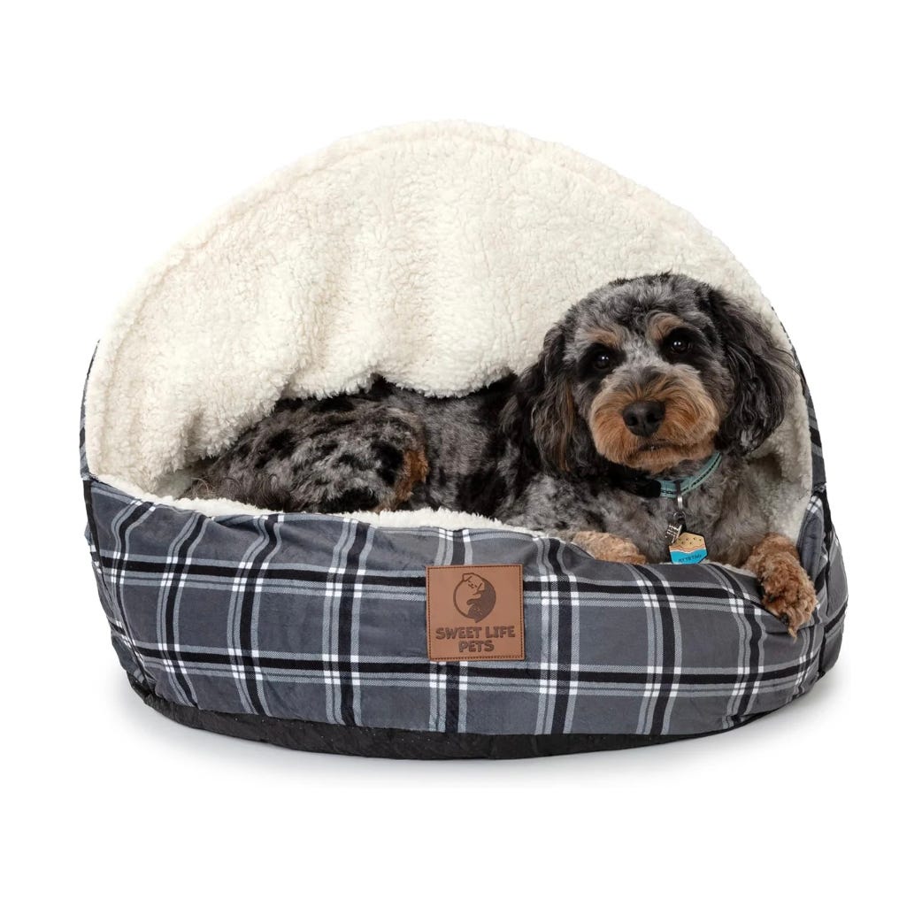 A dog is lying comfortably in a fleece-lined plaid dog bed with a half-dome cover.