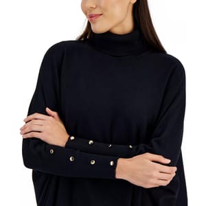 A woman wearing a black turtleneck sweater featuring metallic button details on the sleeves, with her arms crossed.