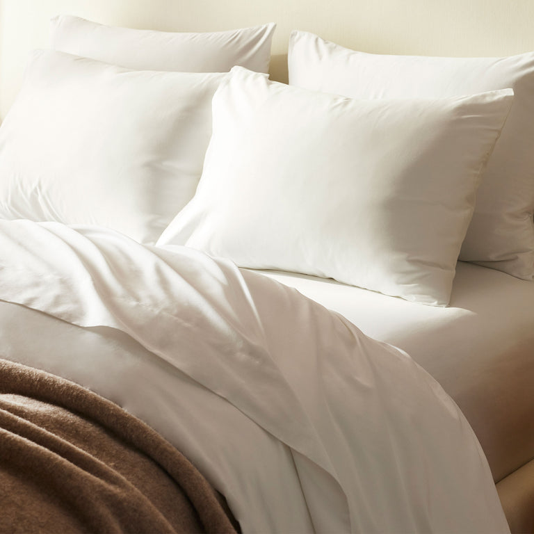 A neatly made bed with two large white pillows, a white duvet, and a brown blanket folded at the foot.