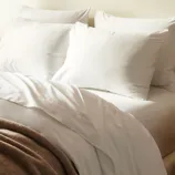 A neatly made bed with two large white pillows, a white duvet, and a brown blanket folded at the foot.