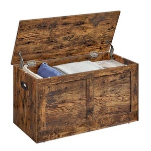 A rustic wooden storage chest with an open lid, revealing a blue pillow, a folded blanket, and a book inside. It features metal hinges and side handles for easy portability.